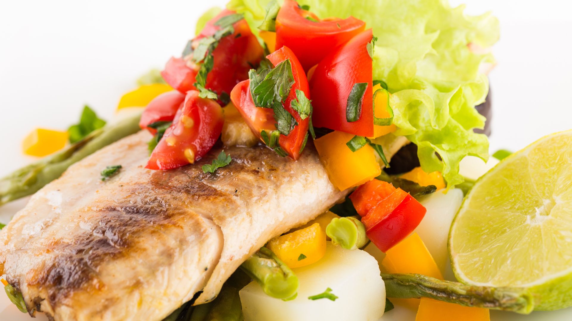 Savor a grilled fish fillet crowned with chopped tomatoes, bell peppers, and herbs on a crisp lettuce bed, accompanied by asparagus, potatoes, and a lime wedge—a delightful taste of what Playa del Coco restaurants have to offer.